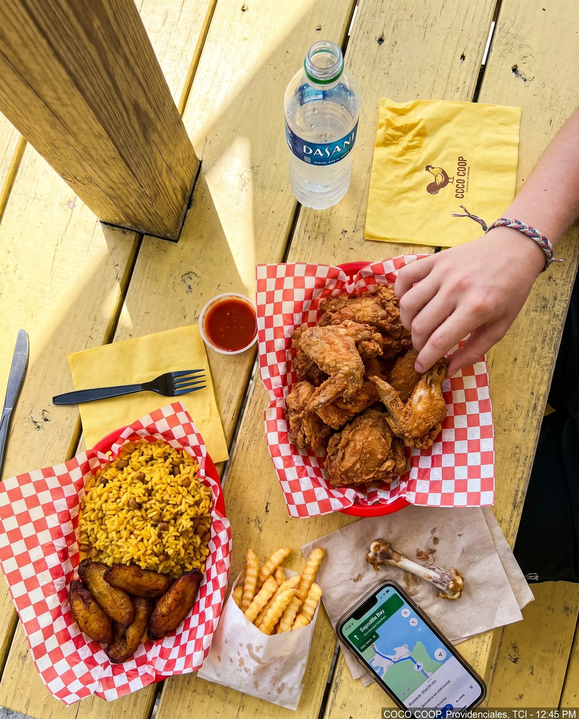 Overhead iPhone photograph of fried chicken, yellow rice, plantains and Dasani water on a COCO COOP picnic table