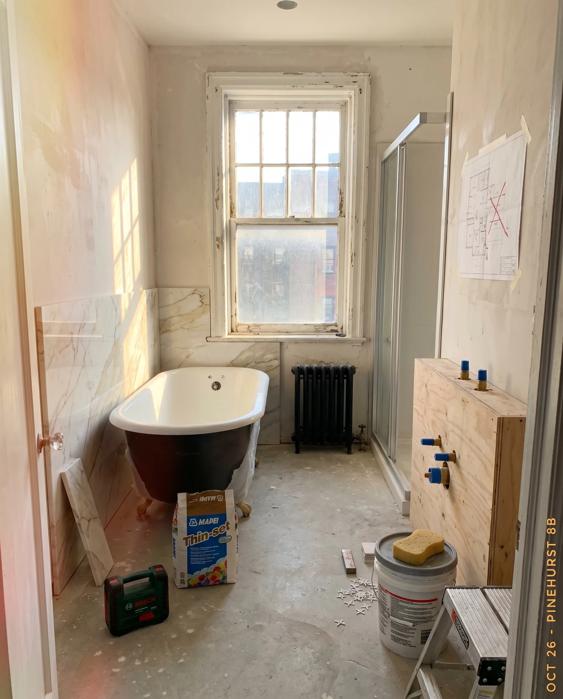 Bookmatched Calacatta gold marble panels being installed in the PINEHURST 8B master bathroom with a wrapped freestanding tub